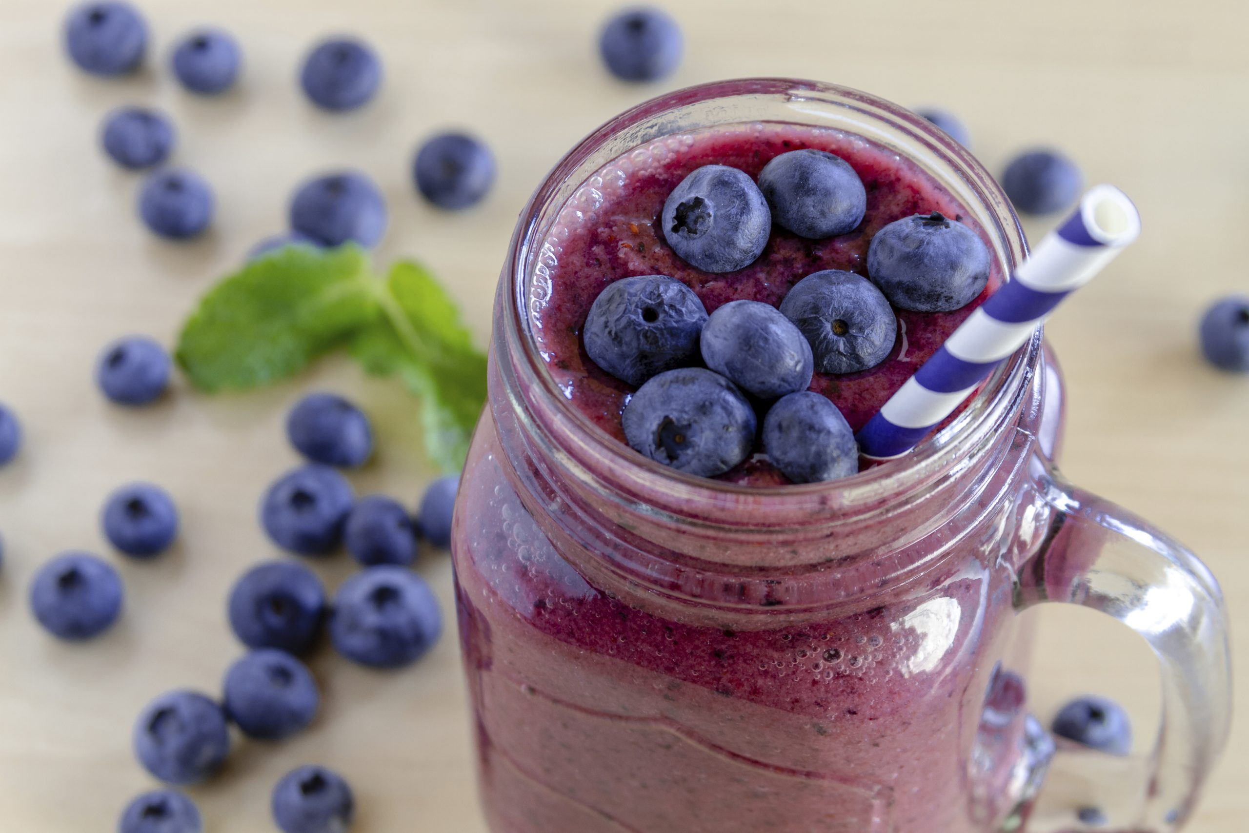 Mason jar filled with blueberry and blackberry fresh fruit smoothie sitting on counter with bowl of blueberries